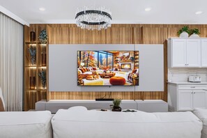Sala de estar moderna com uma televisão de tela plana grande fixada em uma parede de madeira, um sofá branco e um lustre.