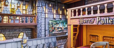 A themed room with a stone wall, a Harry Potter sign, a bookshelf, and a window displaying a room interior.