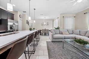A modern kitchen with a central island, dining area with chairs, a sofa, and a glass coffee table. - 4BR house with private pool in Storey Lake (Kissimmee)