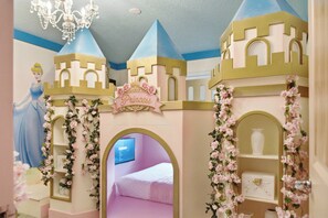 Une chambre décorée sur le thème des princesses, avec un lit, un lustre et une structure rappelant un château.