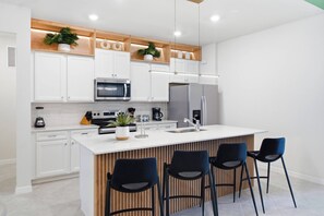 Une cuisine moderne avec des meubles blancs, un îlot central doté de tabourets et des appareils électroménagers intégrés.