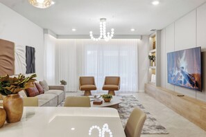 A modern living room with a dining table, two leather chairs, a chandelier, a sofa, a TV, and a large window with curtains. - 8BR house sleeps 22 near Disney area (Clermont)