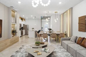 Une cuisine moderne dotée d’appareils électroménagers intégrés, un coin repas avec une grande table et des chaises, et un salon avec un canapé et une table basse.