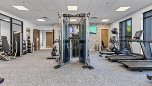 Ein Fitnessstudio mit Laufbändern, Kraftgeräten und einem an der Wand montierten Fernseher.