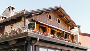A building with a wooden facade, a balcony with potted plants, and a stone chimney.