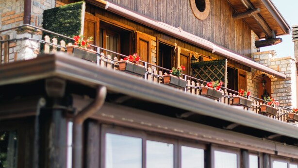 A wooden building with a balcony, large windows, and potted plants.