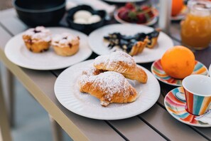 A table with plates of pastries, a bowl of cream, and a glass of orange juice.