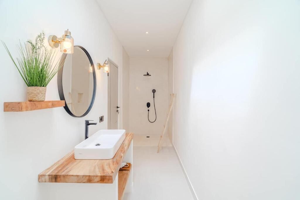 A modern bathroom with a wooden vanity, a round mirror, a potted plant, and a shower.