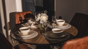 Una mesa redonda para comer con cuencos blancos, copas de vino y un florero con flores blancas.