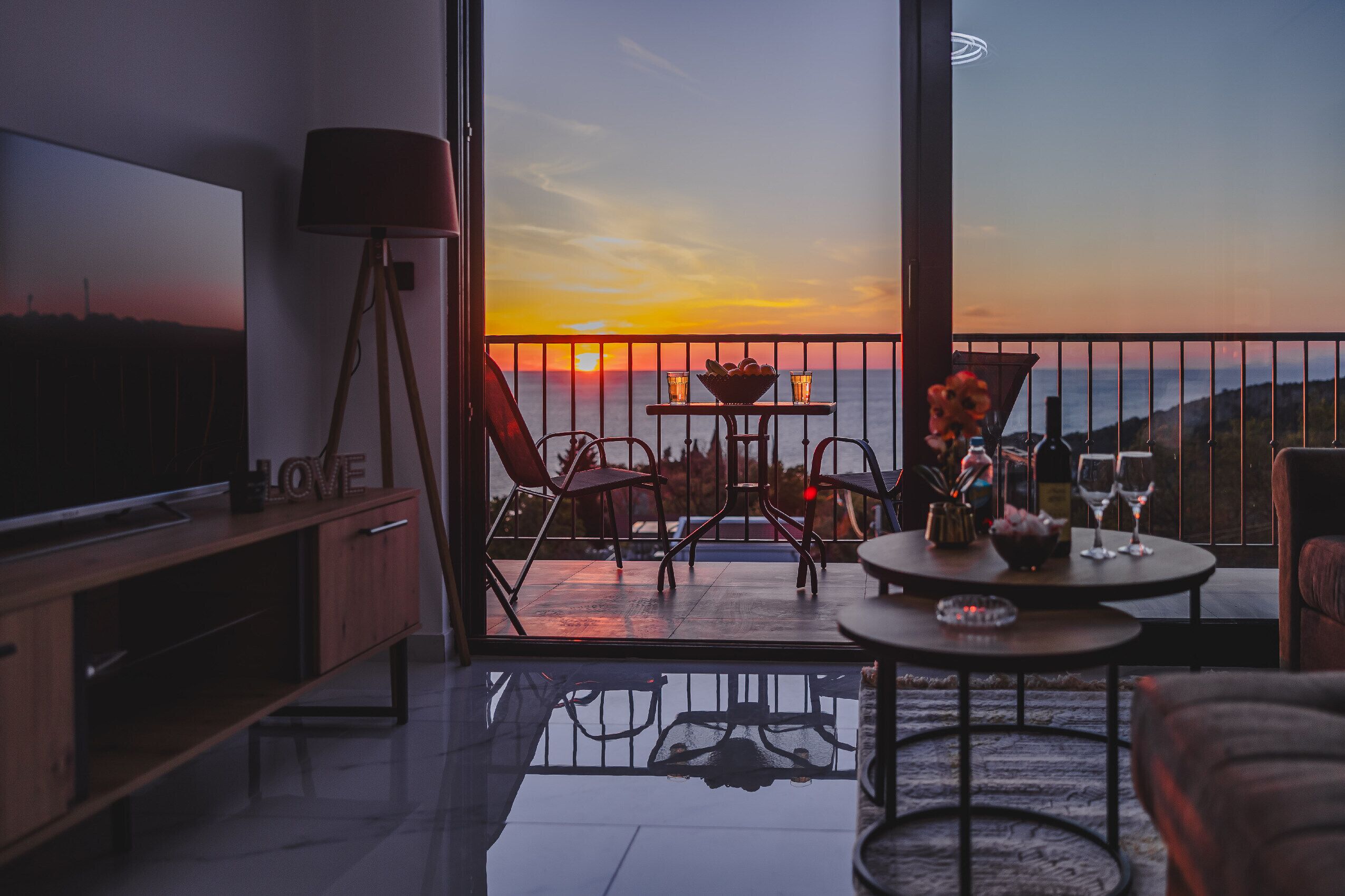 Un balcon avec un téléviseur, une table avec des verres et une vue sur le coucher de soleil.