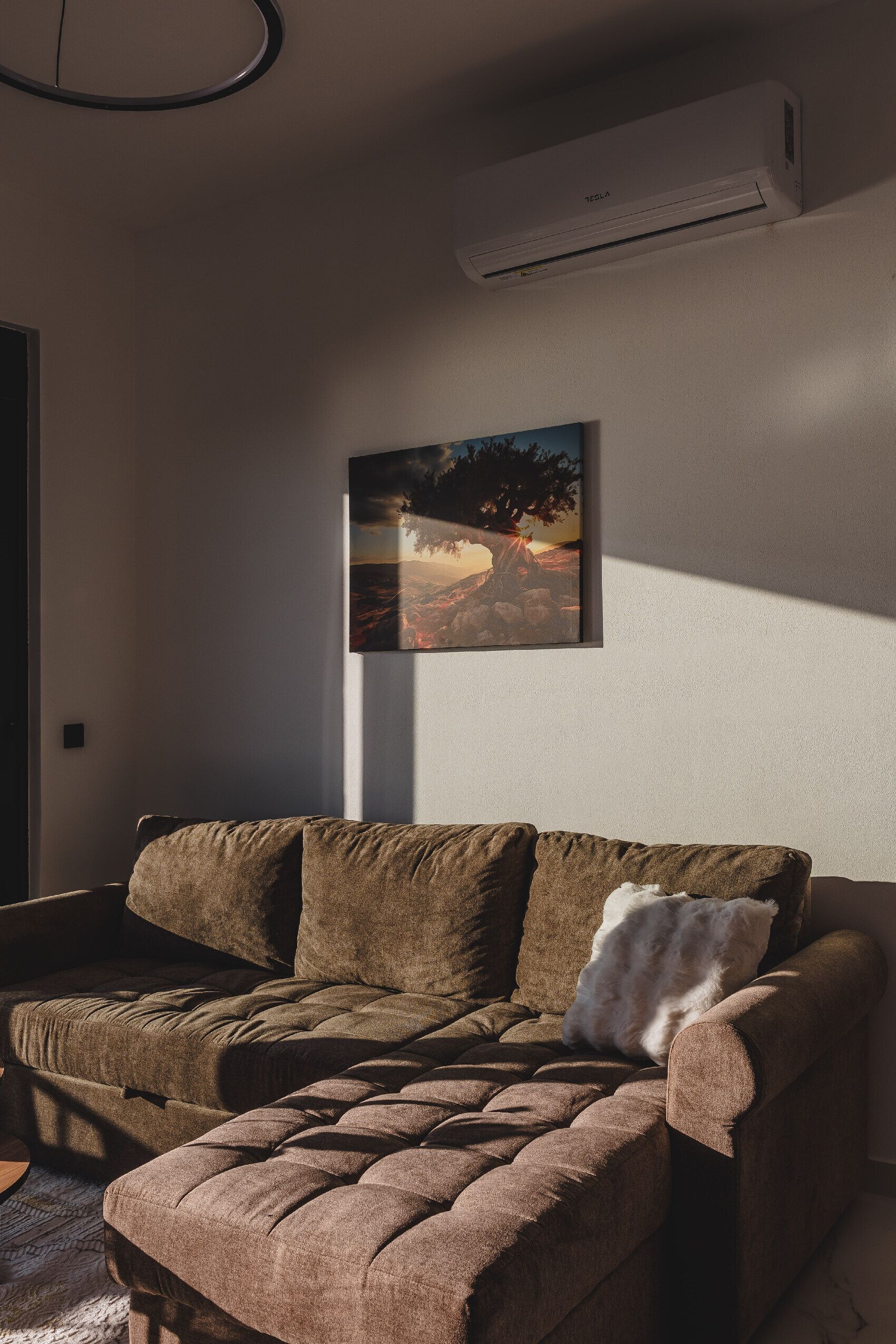 Una sala de estar con un sofá marrón, una almohada blanca y un cuadro en la pared.