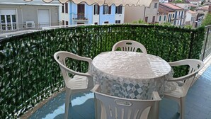 Un balcon avec une table et des chaises, une haie verdoyante et une vue sur des immeubles.