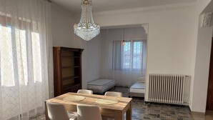 Un coin repas comprenant une table en bois, quatre chaises, un lustre, une bibliothèque, un radiateur et une fenêtre avec des rideaux.