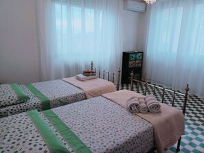 Una habitación de hotel con dos camas, suelo a cuadros, un armario y una ventana con cortinas translúcidas.