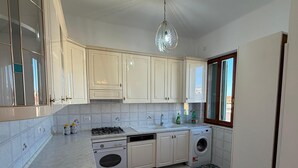 Une cuisine avec des meubles blancs, une cuisinière à gaz, un lave-vaisselle, une machine à laver, un évier et un tapis à motifs.