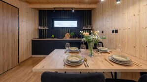 A dining area with a wooden table set for four, a black wall with a window, and a kitchen area in the background.
