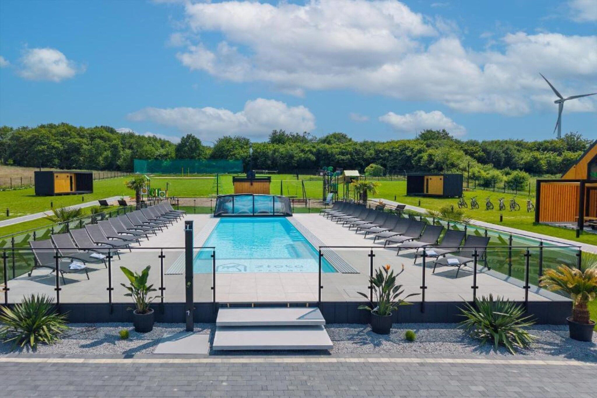 Une piscine dotée d’une terrasse ensoleillée, entourée de chaises longues et de plantes en pot.