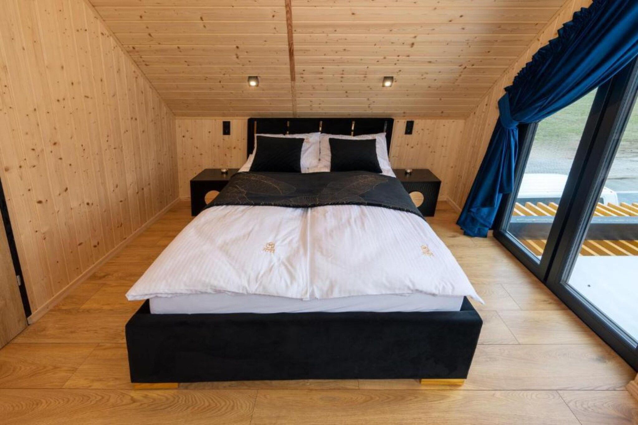 A wooden-paneled room with a bed, two bedside tables, and a window with curtains.