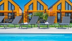 Ein modernes Hotel mit drei Holzbauten, einem Schwimmbad und Liegestühlen.