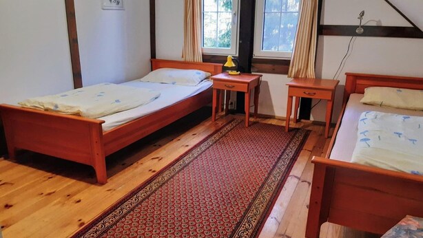 Ein Zimmer mit zwei Holzbett, einem kleinen Tisch mit Lampe und einem Fenster mit Vorhängen.