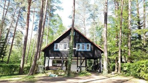 Eine Holzhütte mit Satteldach, umgeben von hohen Bäumen, und ein unbefestigter Weg, der zum Eingang führt.
