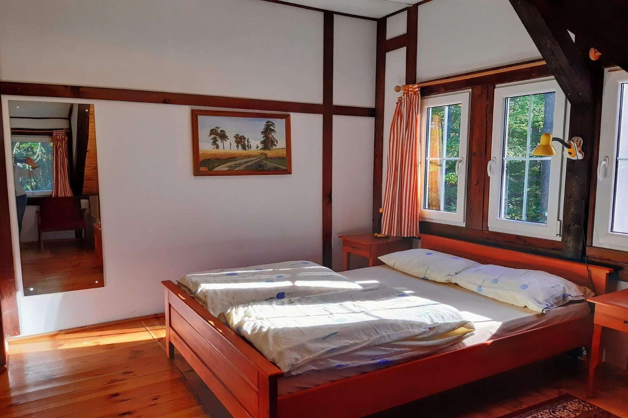 A bedroom with a wooden bed, a painting on the wall, and a window with curtains.