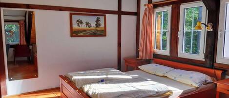 A bedroom with a wooden bed, a painting on the wall, and a window with curtains.
