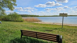 A bench in a grassy area with a lake and a signpost in the background. - Holiday villa with sauna, close to the lake (Nowa Kaletka)