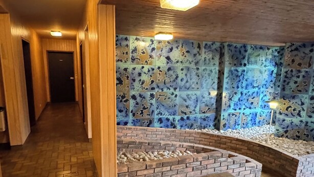 Käytävä, jonka seinät ovat puuta, lattia on koristeltu kalanruotokuviolla ja yhdessä seinässä on sinisiä laattoja sekä tiilimuuri.