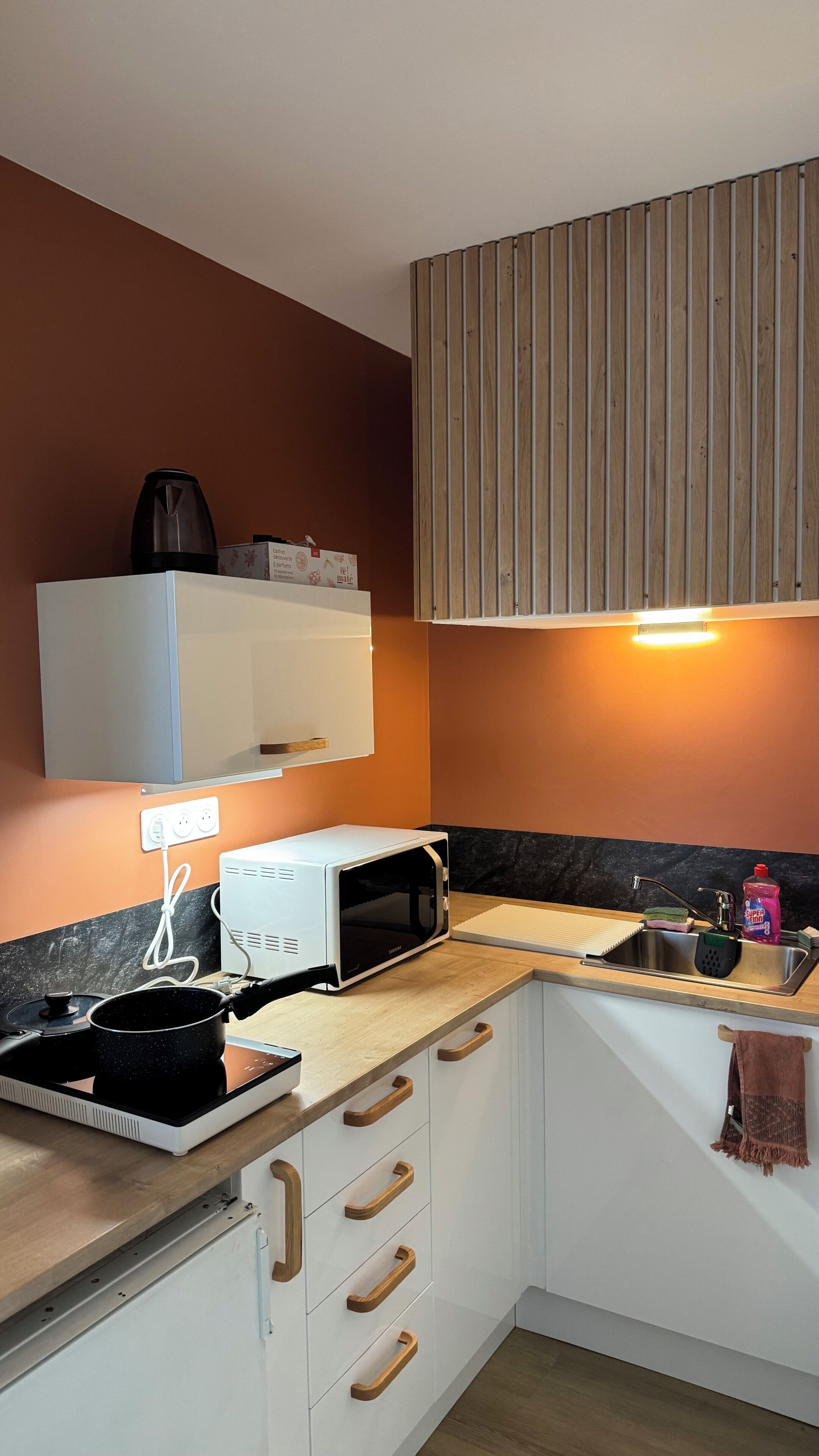 Een kleine keuken met een magnetron, fornuis en houten keukenkastjes.