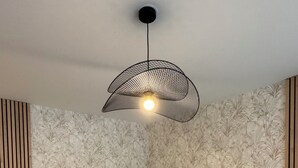 Huoneessa on kaksi sänkyä, kuviollinen tapetti, riippuvalaisin ja puupanelointi.