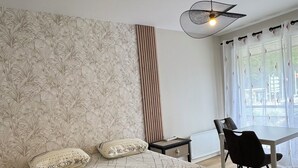 Makuuhuoneessa on suuri sänky, yöpöytä, tuoli, ikkuna, jossa on verhot, ja kattovalaisin.