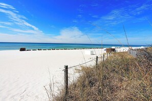Ein Strand mit weißem Sand, einer Holzzahlung und einem strahlend blauen Himmel.
