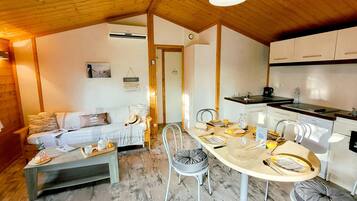 Una habitación acogedora con sofá, una mesa de comedor para cuatro personas, cocina con armarios blancos y techo de madera.