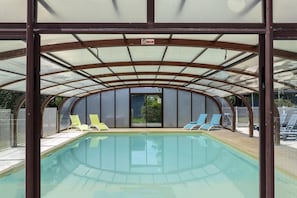 Une piscine intérieure dotée d’un toit couvert, de parois en verre transparent et de plusieurs chaises longues.