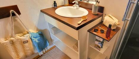 A bathroom with a sink, mirror, towel rack, and a shower area.