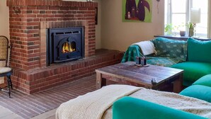 Una sala de estar con chimenea de ladrillo, televisor montado en la pared y un sofá verde.