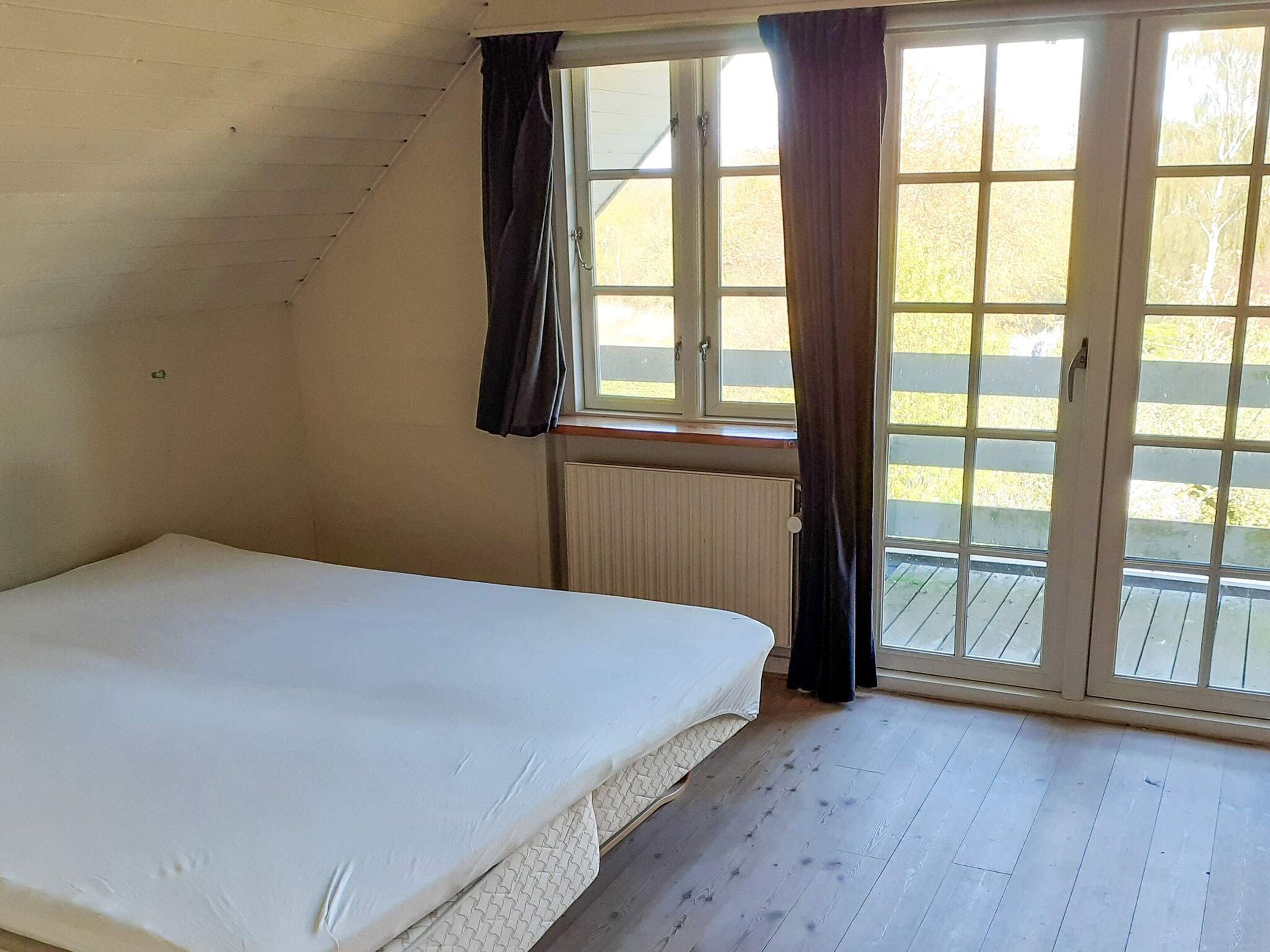 Une chambre avec un lit, une fenêtre avec des rideaux et une vue sur l’extérieur.