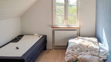 Un alojamiento pequeño y de una sola habitación, con techo inclinado, ventana con vista a follaje, cama con colcha colorida y escritorio con silla.