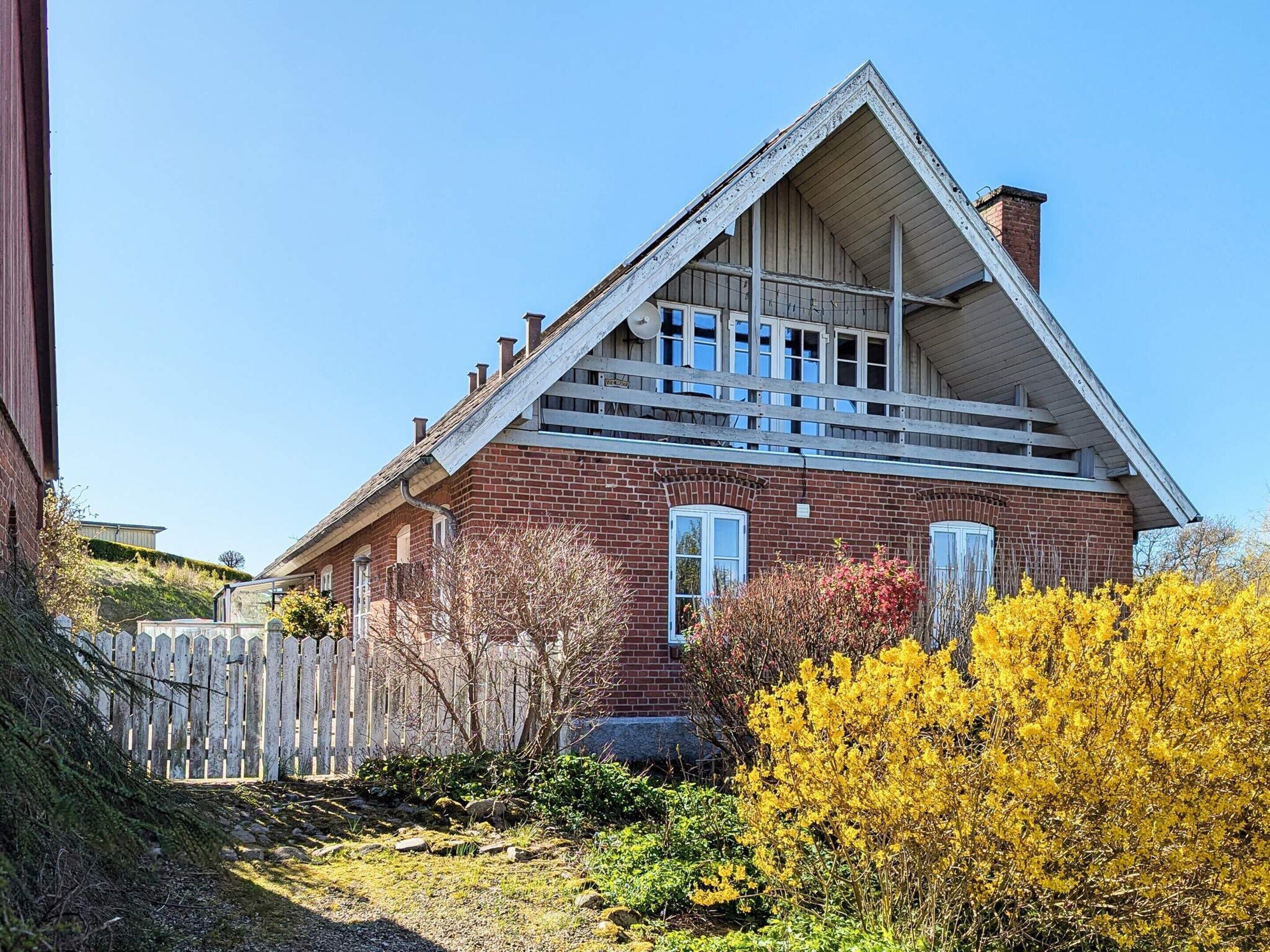 Et rødt murstenshus med tagkvist og træterrasse.