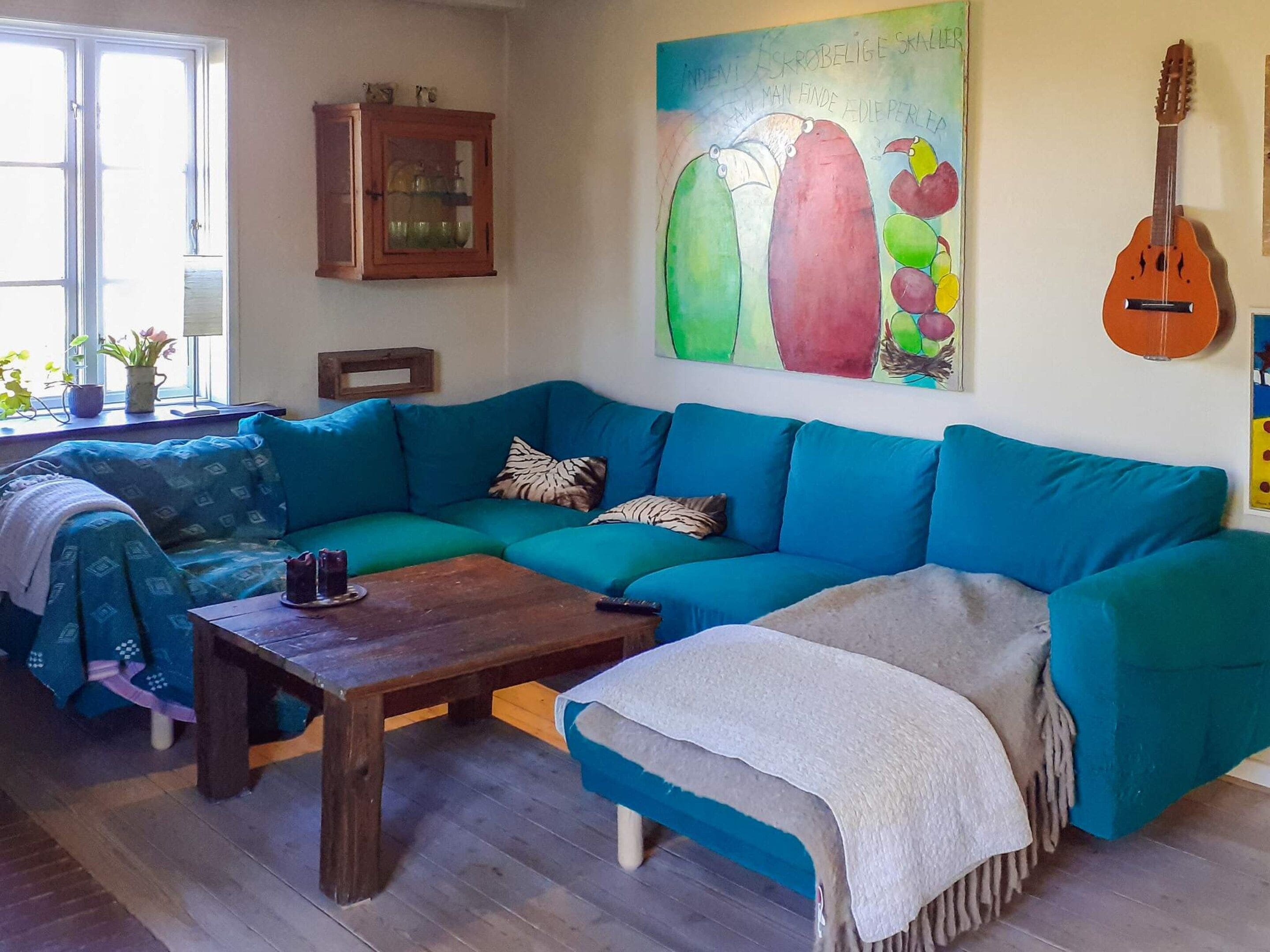 Una sala de estar con un sofá verde azulado, una mesa de centro de madera y un cuadro en la pared.