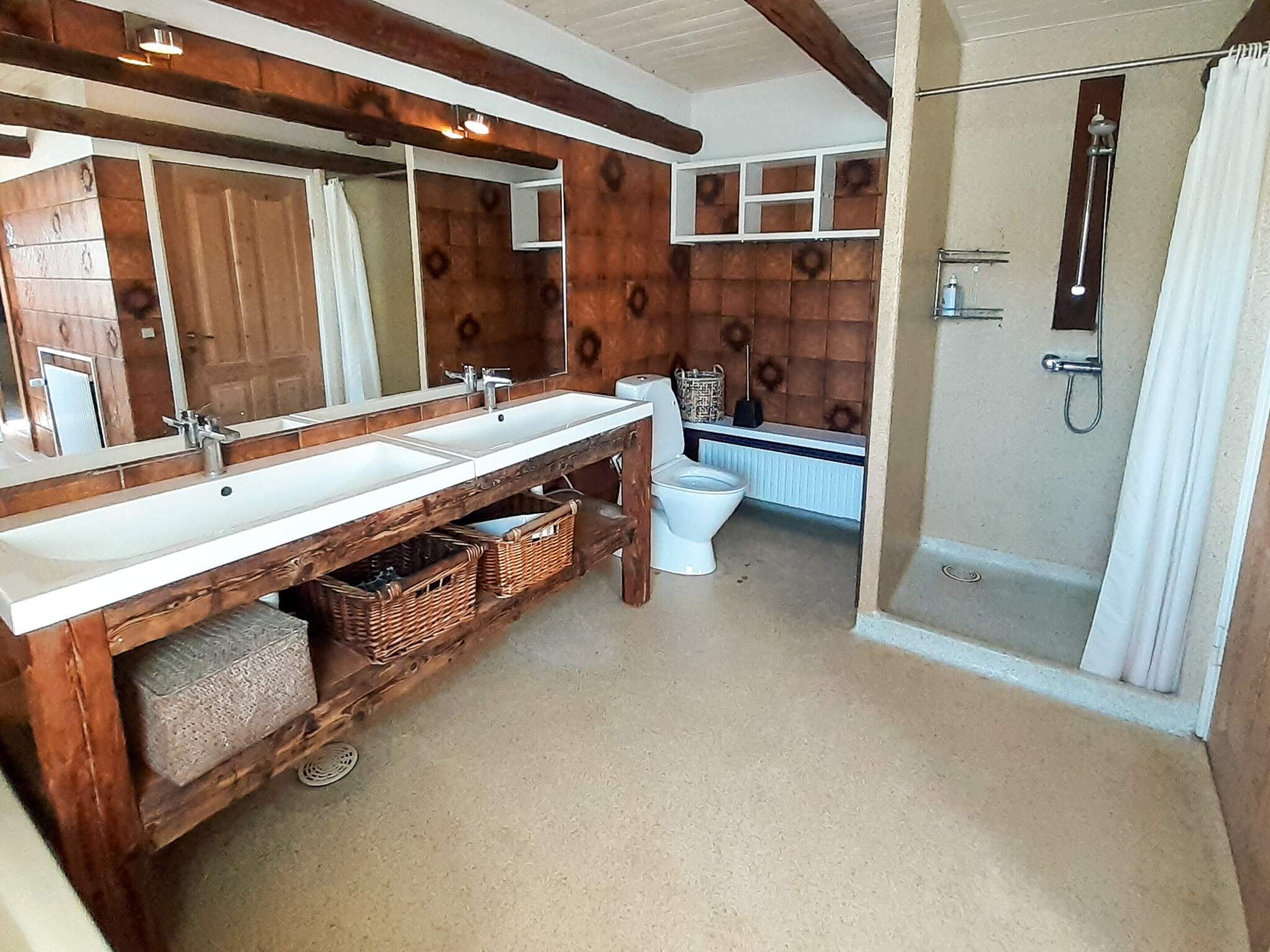 Een badkamer met een houten wastafelmeubel, twee wasbakken, een toilet en een douchegedeelte.