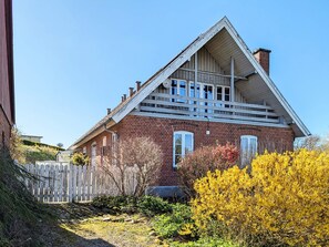 Uma casa de tijolos de dois andares, com telhado em duas águas e varanda frontal.