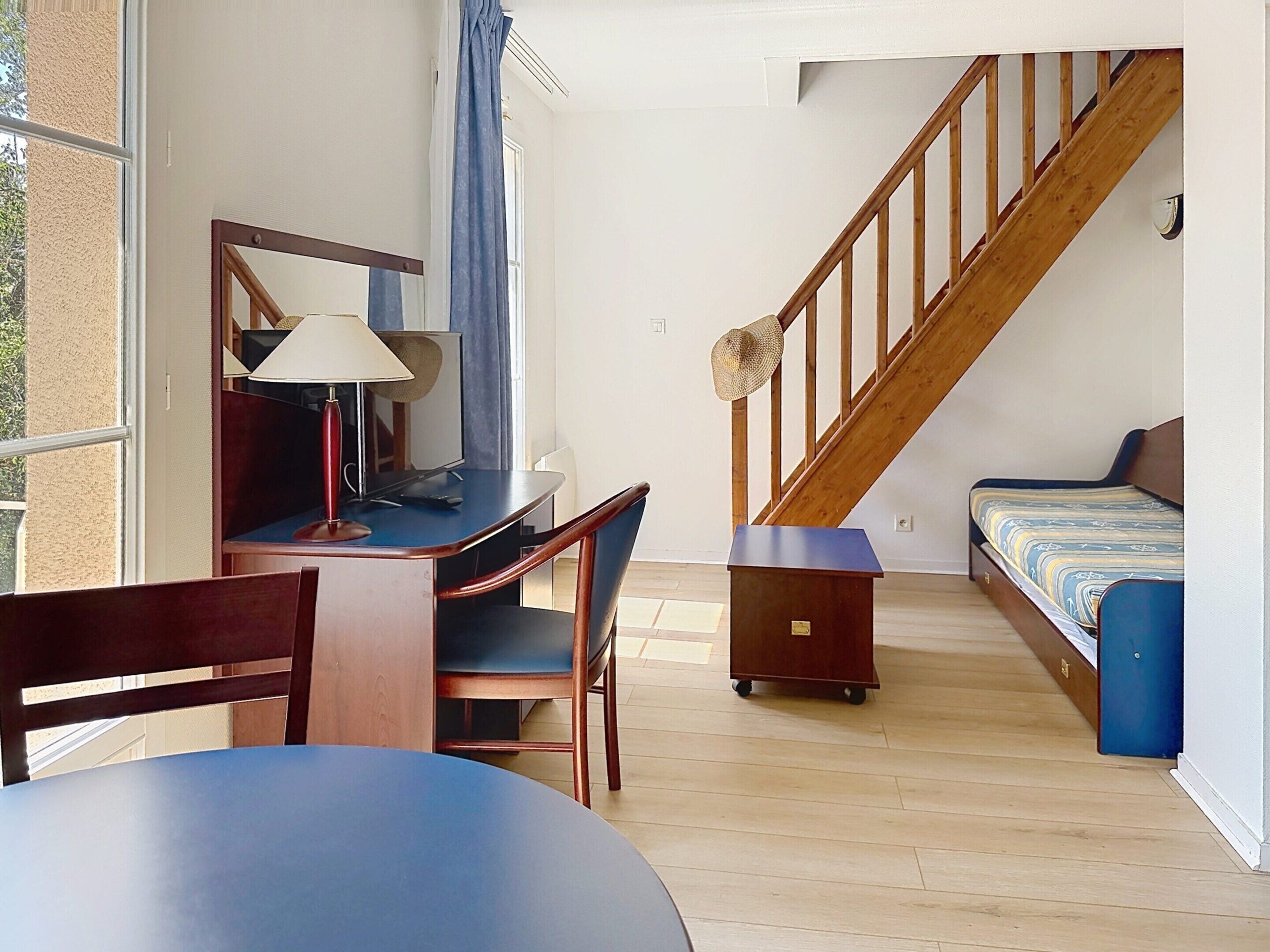 Een kamer met een bureau, stoel, bed en een houten trap.