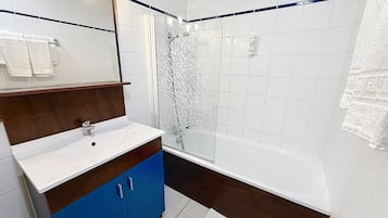 A bathroom with a white sink, blue cabinet, and a glass-enclosed shower.
