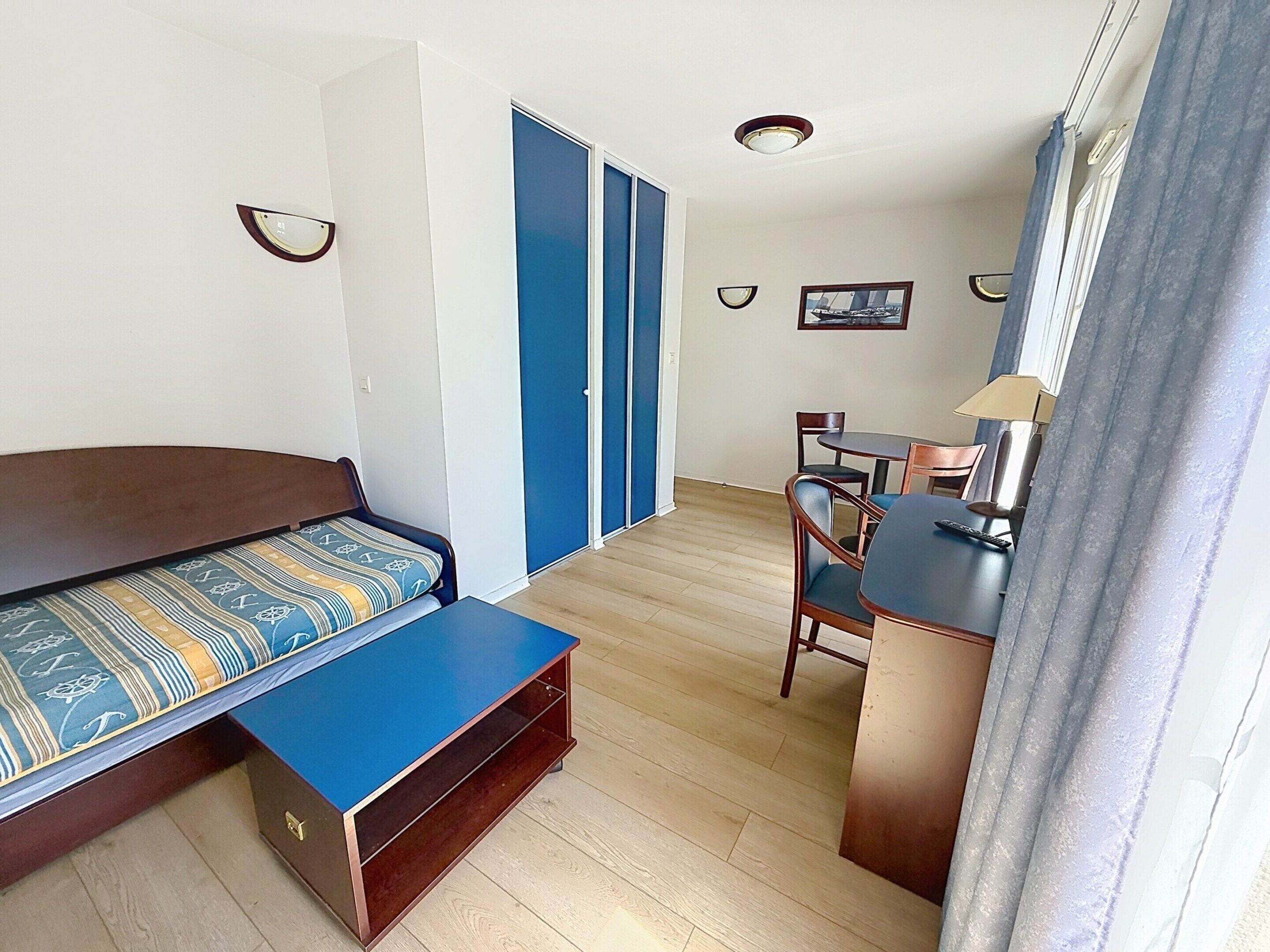 A compact room with a bed, a desk, and a chair. There is a door with a blue frame and a picture on the wall.