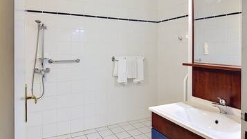 Een badkamer met witte betegelde wanden, een douche met handdouche, een wastafel met spiegel erboven en een handdoekrek met twee witte handdoeken.