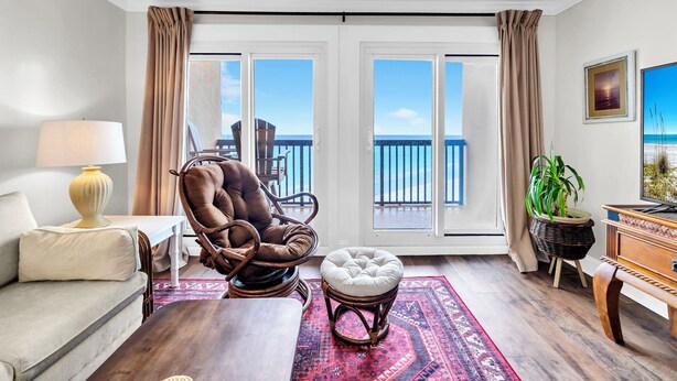 Ein Wohnzimmer mit Sofa, Sessel, Hocker, Lampe und Blick auf den Ozean durch große Fenster.