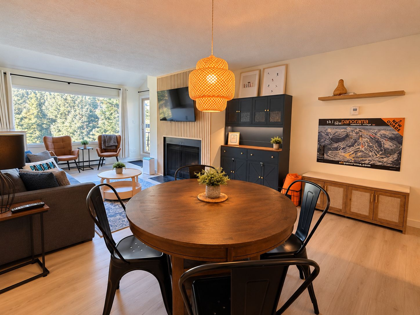 Una sala moderna con una mesa de comedor redonda de madera, sillas negras, un sofá y un televisor montado en la pared.