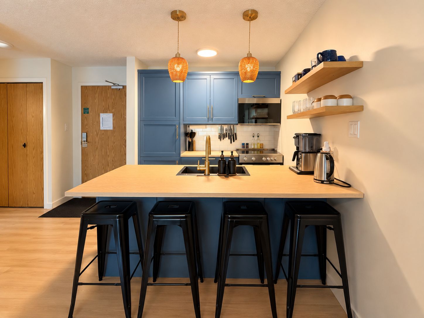 A modern kitchen with blue cabinets, a central island with stools, and pendant lighting.